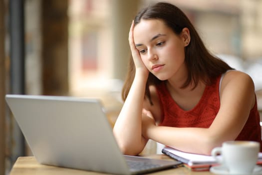 Apathetic student watching online content on laptop in a coffee shop terrace
