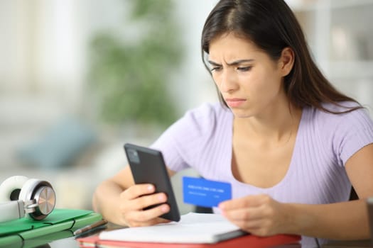 Worried student buying online with credit card and phone at home