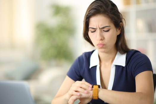 Worried woman checking smartwatch sitting at home