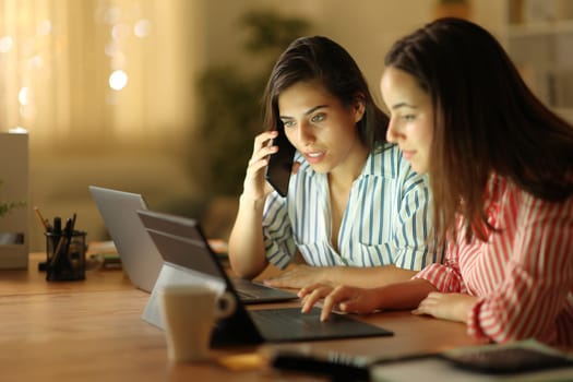 Two tele workers talking on phone solving online problem in the night at home