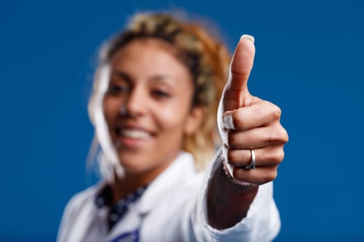 Focus on thumbs-up with manicured nails of competent brown-skinned doctor, who's smiling, approving, reassuring. Keep going with the care!