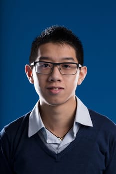 Mugshot of an Asian man with glasses, disheveled shirt, and a blue sweater on a blue background. Every individual has their own story