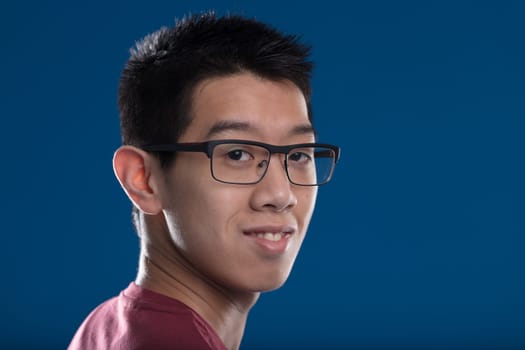 Smiling East Asian youth in glasses, his burgundy shirt contrasting the blue background. His short hair and the image exude an aura of positive future and fortune