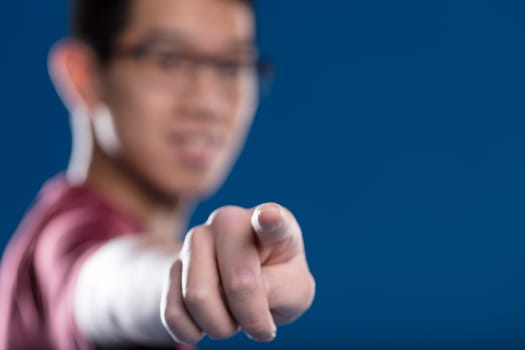 Fingertip on a transparent screen in sharp focus, blurry Asian man with glasses in the backdrop on blue. Ideal for touch graphic applications