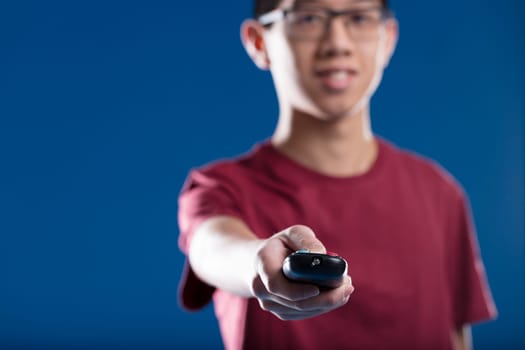 focused forefront of a remote control for a TV or home appliance like a vacuum robot or an air conditioner. Comfortably controlling your machines with the blurred happy face of an Asian individual hol