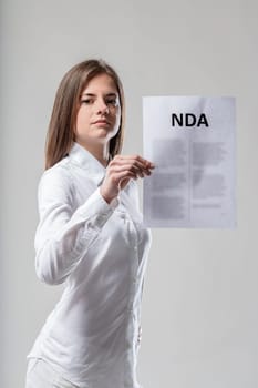 Focus on NDA, held by woman in white, warning about speech restriction. Attention: signing means limited freedom of expression