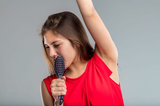 Young woman in red dress sings passionately pretending her hairbrush is a microphone, she is very much into the part and happy