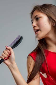 Young woman in red dress sings passionately pretending her hairbrush is a microphone, she is very much into the part and happy