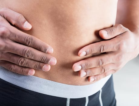 Close-up of a man's hands resting on his belly. Self-conscious, he feels overweight and aims to improve his lifestyle