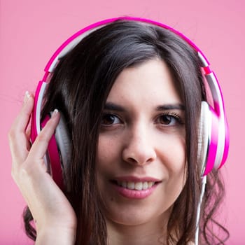 A woman seriously absorbed in music and podcasts, gently laughs, relaxing. Her pink headphones on a colorful background