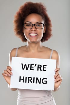 Enthusiastic woman holds a 'We're Hiring' sign, her bright smile inviting potential applicants