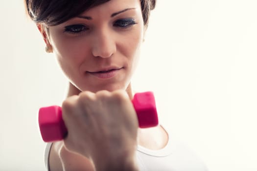 Young woman working out with weights concentrating on a routine staring down at the dumbbell in her hand with determination
