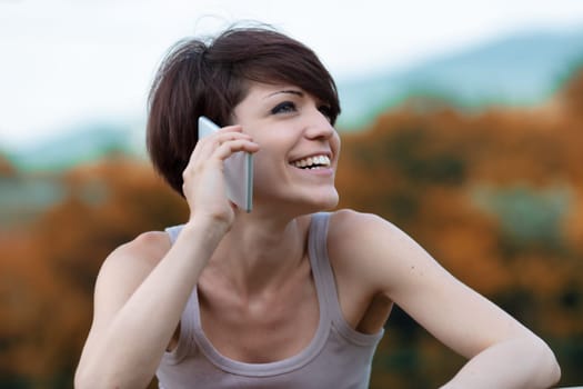 Happy young woman relaxing outdoors talking on her mobile phone listening to the conversation with a vivacious grin in a close up portrait