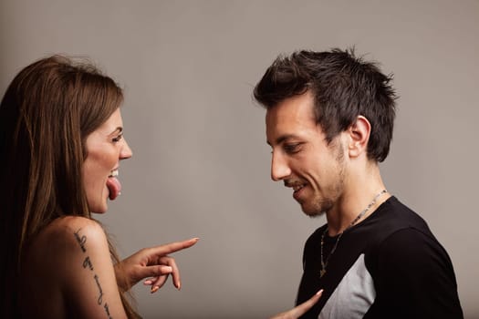 A young woman playfully taps her boyfriend's chest, he tolerates with patience, adoring her antics. She teases him childishly, her heart brimming with love, in a lively moment foretelling a burst of e
