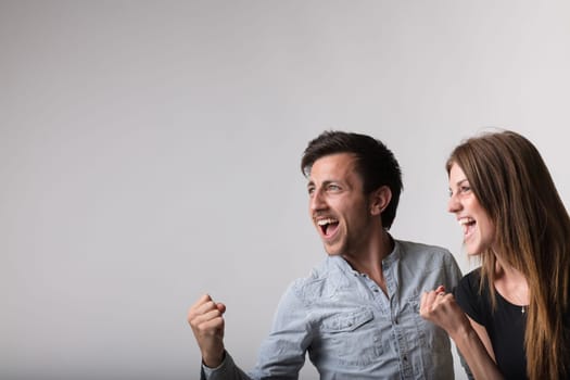 A man and woman, framed in a corner, exude joy and passion with fists raised in victory. Facing the copyspace, their side profiles radiate success, positivity, and celebratory laughter