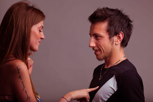 A young woman playfully taps her boyfriend's chest, he tolerates with patience, adoring her antics. She teases him childishly, her heart brimming with love, in a lively moment foretelling a burst of e