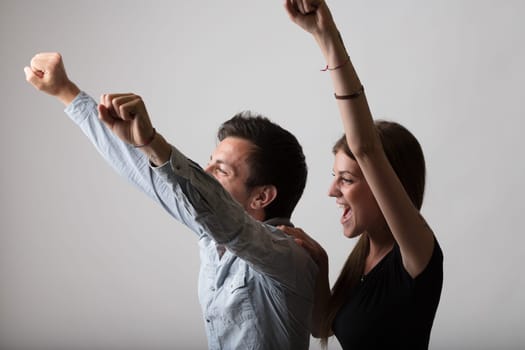 A man and woman on a neutral background exude joy and exultation to the side, raising their arms, smiling and shouting for victory and success. The scene radiates enthusiasm and satisfaction