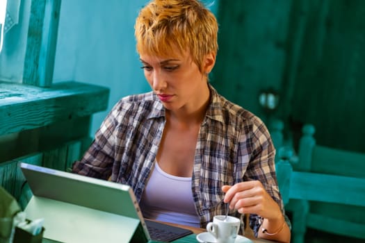 Woman in plaid immerses in her tablet-laptop, a fusion of tradition and tech in a wooden café