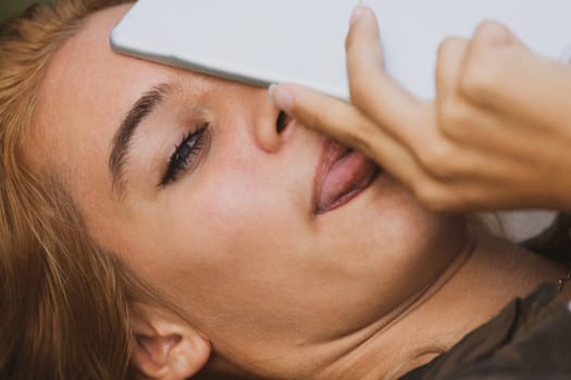 Cheeky young woman makes a playful gesture with tongue, tablet in face