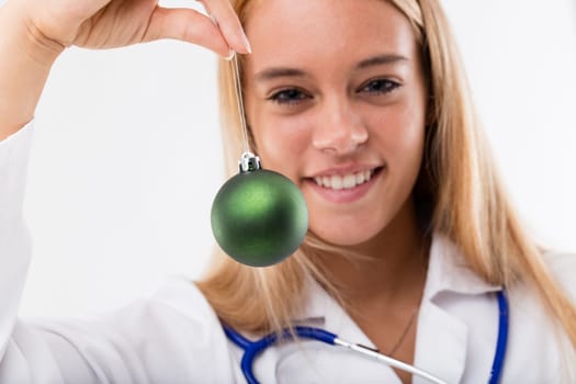concept of doctors at Christmas time a smiling young blond doctor holds a green Christmas bauble in the foreground