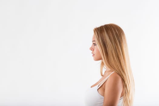 Side portrait on neutral background of blond girl in white tank top looking serious in front of her large copyspace on left