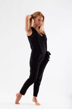 Fashion portrait of a young blond woman in a black jumpsuit she is barefoot and has her hands in her pockets