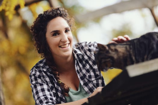 In a public park, a woman in a black-and-white plaid shirt is petting and cuddling a big cat she found. He enjoys the pleasure because cats know how to do that.
