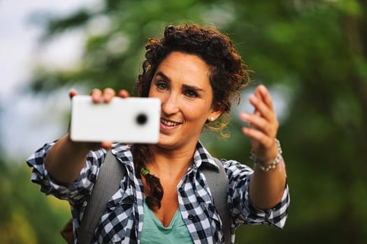 Human photographer is taking cell phone pictures of someone and giving them directions on how to position themselves in the frame with hand gestures. Beautiful portraits can be taken in nature. Until
