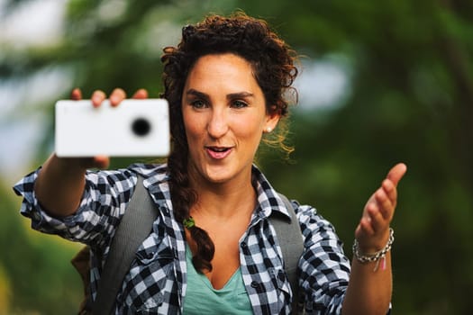 Human photographer is taking cell phone pictures of someone and giving them directions on how to position themselves in the frame with hand gestures. Beautiful portraits can be taken in nature. Until