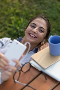 A three-quarter view from above shows a girl lying on her back on a bench, with wired earphones connected to her smartphone. She interrupts herself and smiles at us, sharing her thoughts. She wants us