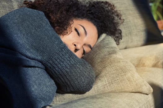 Sunlight graces a beautiful girl with closed eyes on her couch. Curly-haired, wrapped in her warm sweater and home's comfort, she may be dreaming, resting or asleep. She's simply beautiful
