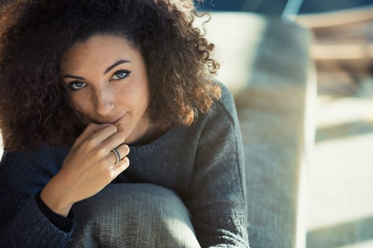 In her sunlit living room, a curly-haired young model lounges on her sofa, reading with one hand at her lips. Her captivating eyes and adorable coy smile radiate charm, as we admire her perfectly mani