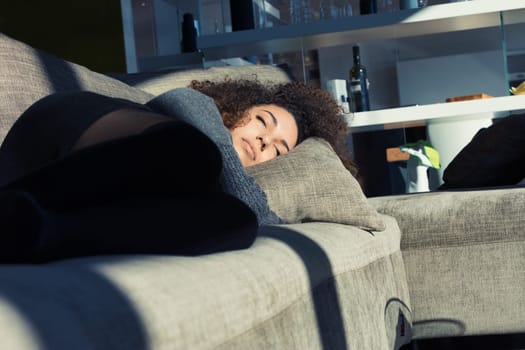Sunlight graces a beautiful girl with closed eyes on her couch. Curly-haired, wrapped in her warm sweater and home's comfort, she may be dreaming, resting or asleep. She's simply beautiful