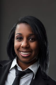 Black woman with a confident smile wearing a white shirt and black tie poses for a professional portrait