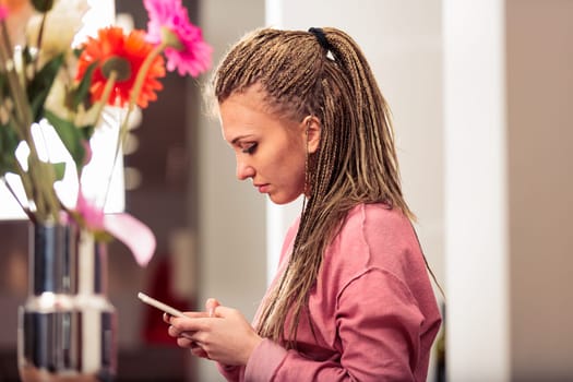 In her kitchen, a girl with box-braid braids in a pink sweatshirt engages with games and apps, modern entertainment