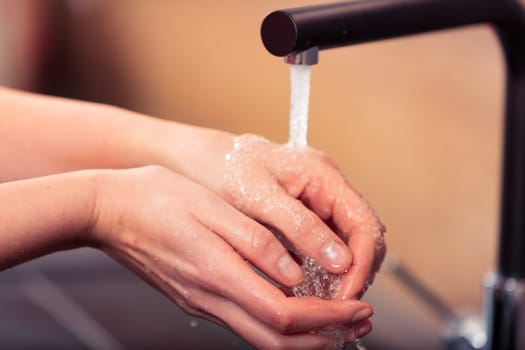 Kitchen faucet over female hands. Highlighting the taken-for-granted luxury of fresh, clean water, and those grateful to pay for it