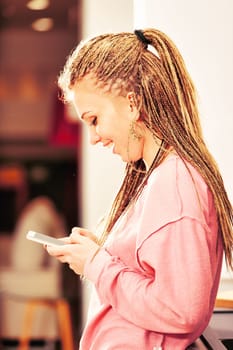 Engrossed in her smartphone, a girl with box-braids in a pink hoodie epitomizes today's digital entertainment