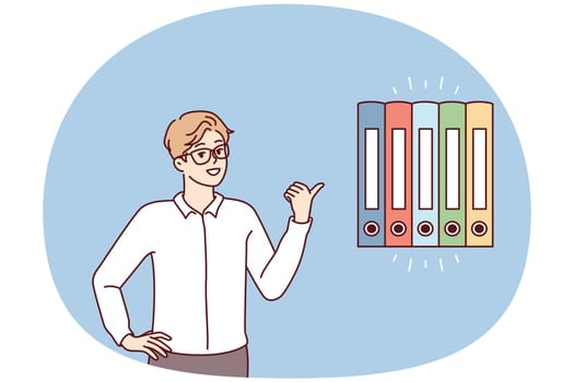 Man office worker points finger at multicolored folders for documents. Guy in business clothes gives advice on finding reports or recommends system for storing financial papers