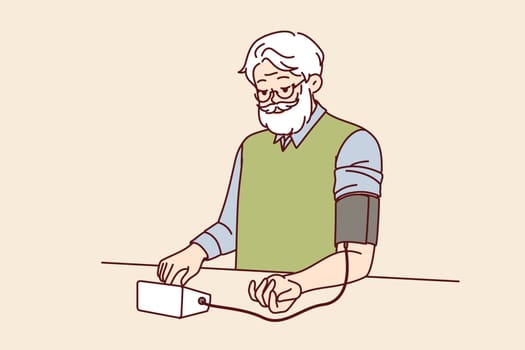 Elderly man measures blood pressure with tonometer, tracking health and cardio indicators. Gray-haired grandfather uses tonometer to decide whether to take pills prescribed by doctor or not.