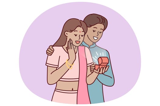 Indian man surprises wife with box of jewelry or engagement ring as token of love and devotion. Guy and girl in Indian national costumes during romantic date or engagement ceremony