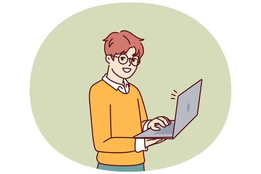 Smart little boy with open laptop for preparing homework assigned from school stands and looks at camera. Schoolboy in casual wear holding laptop using internet and learning software development