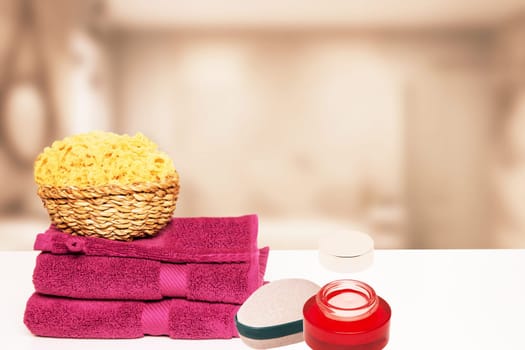 Closeup of fresh soft terry bath towels and soap, shampoo bottles and a basket with a natural sponge on table over blurred bathroom background. Copy space.
