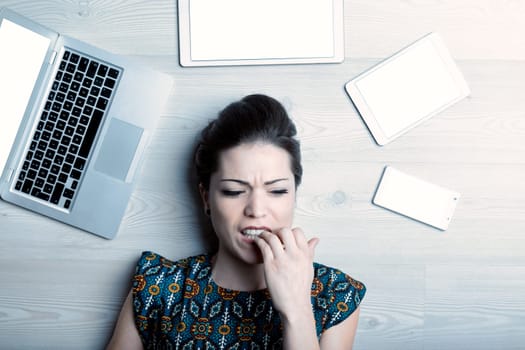 Overhead shot of a young woman, a communication, advertising, graphic design, PR professional. Struggling with creative block, her face is encircled by tablets, smartphones, computers. Copywriting, co