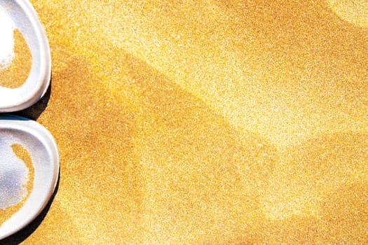 Summer beach background. White shoes or flip-flops on a golden sunny sandy beach. Advertisment travel.