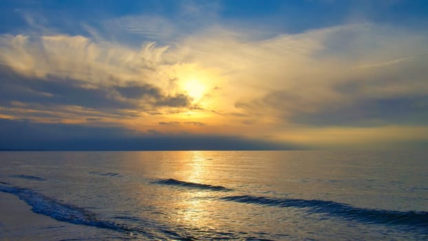 Sunset, illuminated sea. Sandy beach in the foreground. Light waves. Baltic Sea. Landscape on the coast
