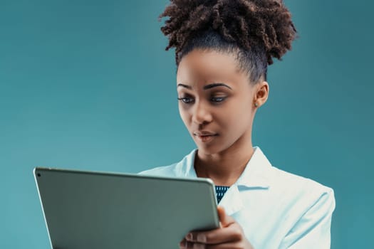 Focused and poised, a woman in a lab coat consults a digital tablet with keen interest