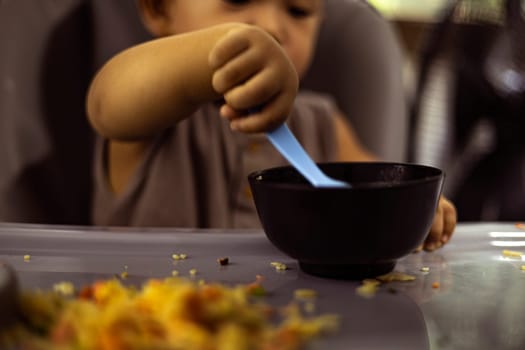 Little Asian boy enjoys eating food by herself. Child development by allowing them to do things by themselves.