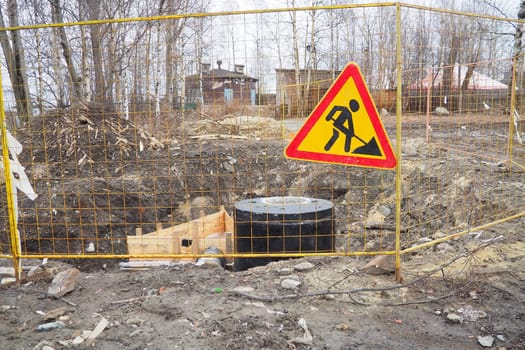 A road works sign warns the driver that he is approaching a section of road where repair work is being carried out. Laying pipes or heating mains. Metal fencing. Development of urban infrastructure.