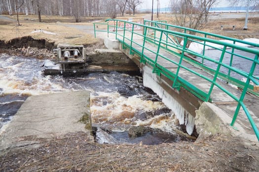 Spring flood. Rushing water in the river. Dark ferrous water rushes in the stream. Karelia, Lososinka River in spring. Floods, tsunami and climate change. Destroyed bridge with pipe. Weather disaster