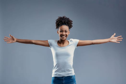 Open-armed young woman in white shirt beams with joy, offering a hug in a friendly manner